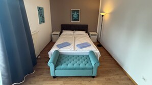 A bedroom with a bed, two bedside tables, a floor lamp, a blue sofa, and two wall art pieces.
