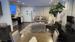 Een moderne woonkamer met een eethoek, met een grote televisie, comfortabele zithoek en een bijzettafel met decoratieve objecten.