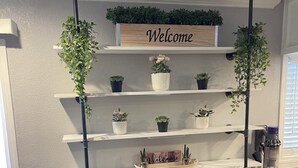 Een receptiegedeelte met een 'Welcome'-bord, meerdere planken met potplanten, twee zwarte afvalbakken en een gestreept stoel.