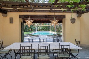 An outdoor patio with a pool, wooden pergola, star-shaped hanging lights, and a table with chairs.