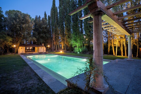 A swimming pool with a pergola and a small pavilion in a landscaped garden.