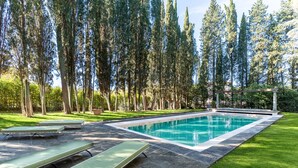 A rectangular swimming pool with a stone border, surrounded by a well-maintained lawn and tall trees. - Villa Loretino - Ultimate Luxury in Florence (Comeana)