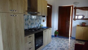 A kitchen with wooden cabinets, a gas stove, and a tiled floor. - Lovers' balcony (Santa Domenica)