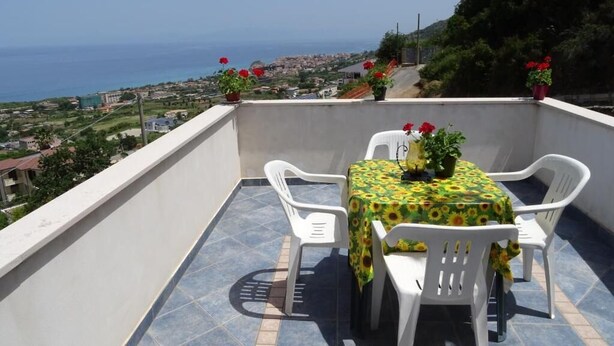A balcony with a table and chairs, a view of the sea, and potted plants. - Lovers' balcony (Santa Domenica)