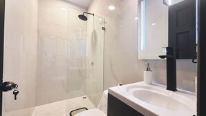 A modern bathroom with a glass-enclosed shower, a white toilet, and a large mirror above the sink.