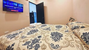 A hotel room with a bed, a TV mounted on the wall, and a door leading to another room.
