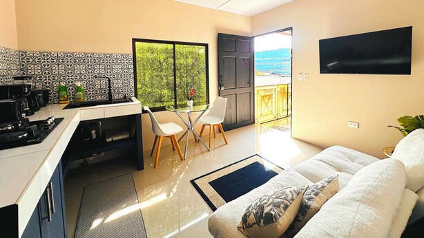 A modern kitchen with a dining area, a TV, and a balcony with a view.