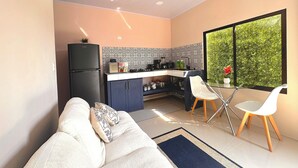 A compact living space with a kitchenette, a dining area with a glass table, and a sofa with cushions.
