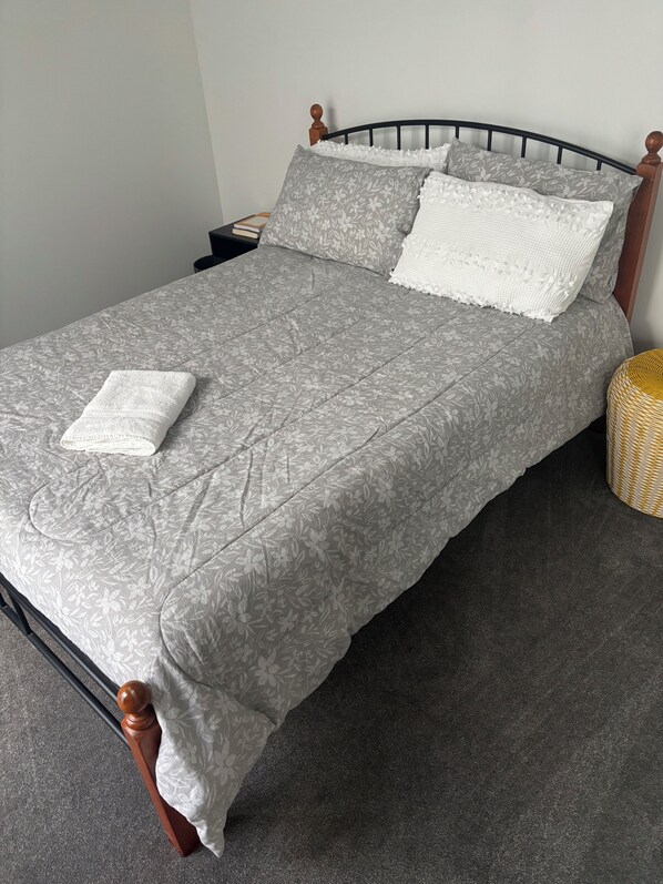 Una cama bien hecha con un edredón floral gris, dos almohadas y una toalla blanca doblada.