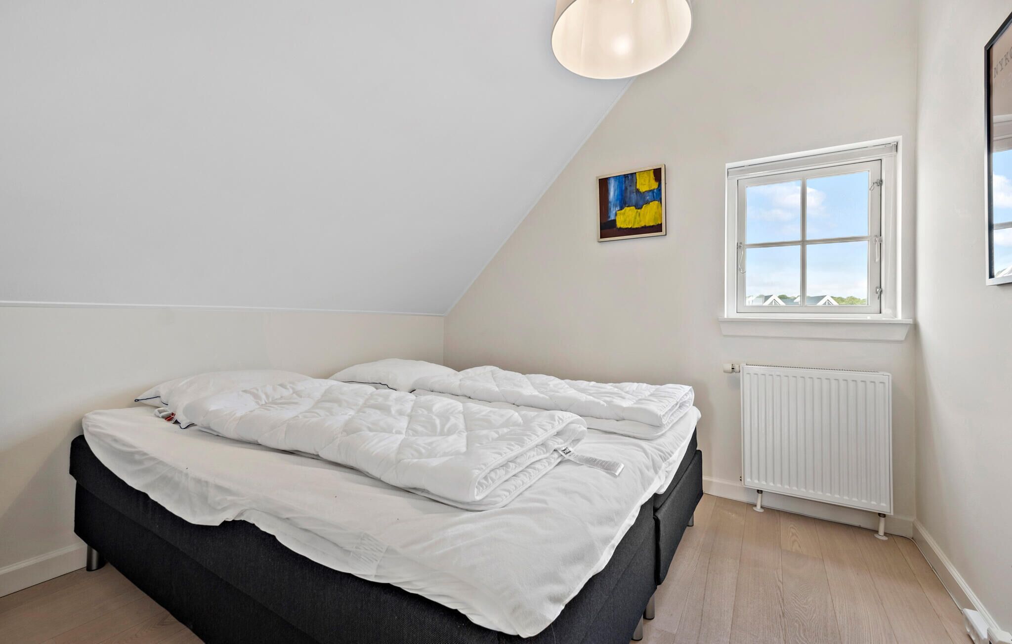 Une chambre à coucher avec un lit, une fenêtre, un radiateur et un tableau accroché au mur.