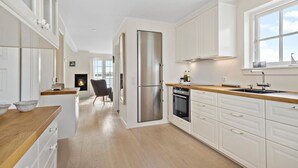 A modern kitchen with white cabinetry, a stainless steel refrigerator, a wooden countertop, and a built-in oven.