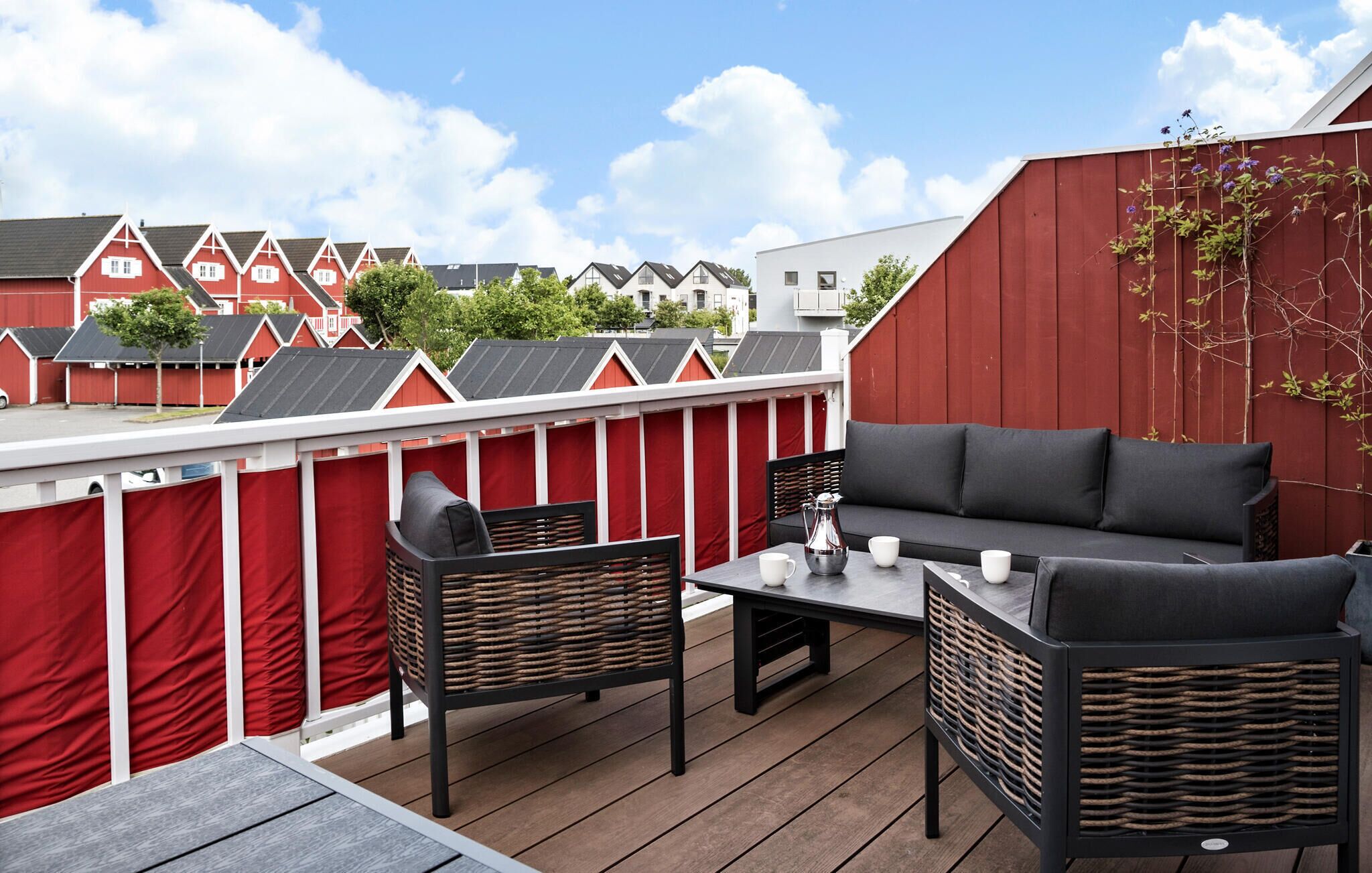 Une terrasse sur le toit, agrémentée d’une clôture rouge et blanche, d’un canapé noir et de fauteuils en osier.