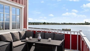 A covered outdoor seating area with a view of a lake, a red and white railing, and a window overlooking the water.