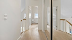 A bright, modern hallway with wooden floors, white walls, and a glass door leading to another room.