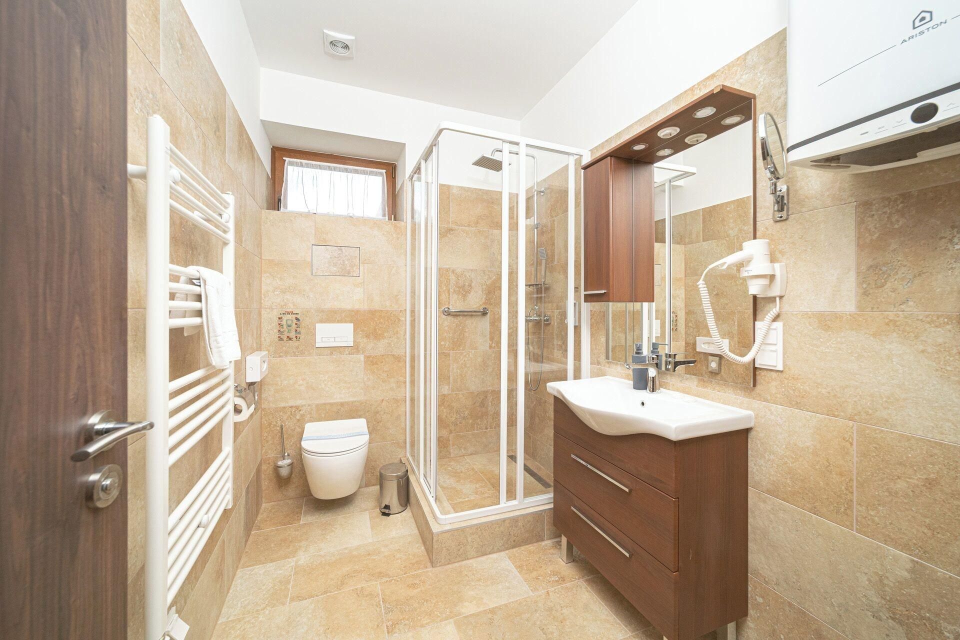 A bathroom with a glass shower enclosure, a toilet, a sink with a mirror, and a hairdryer mounted on the wall.