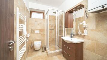 A bathroom with a glass shower enclosure, a toilet, a sink with a mirror, and a hairdryer mounted on the wall.