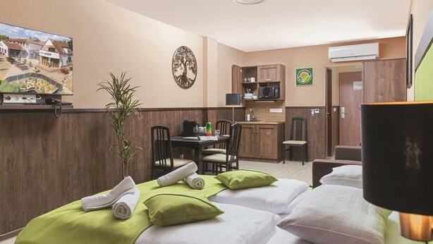 A hotel room with two beds, a small dining table, a kitchen area, and a reception desk. - Parl Hotel Bükfürdő (Buk)