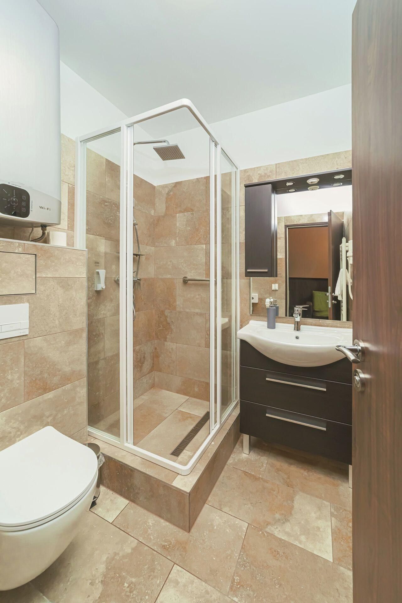 Un baño moderno con ducha de vidrio, inodoro blanco, lavamanos con espejo y tocador oscuro.