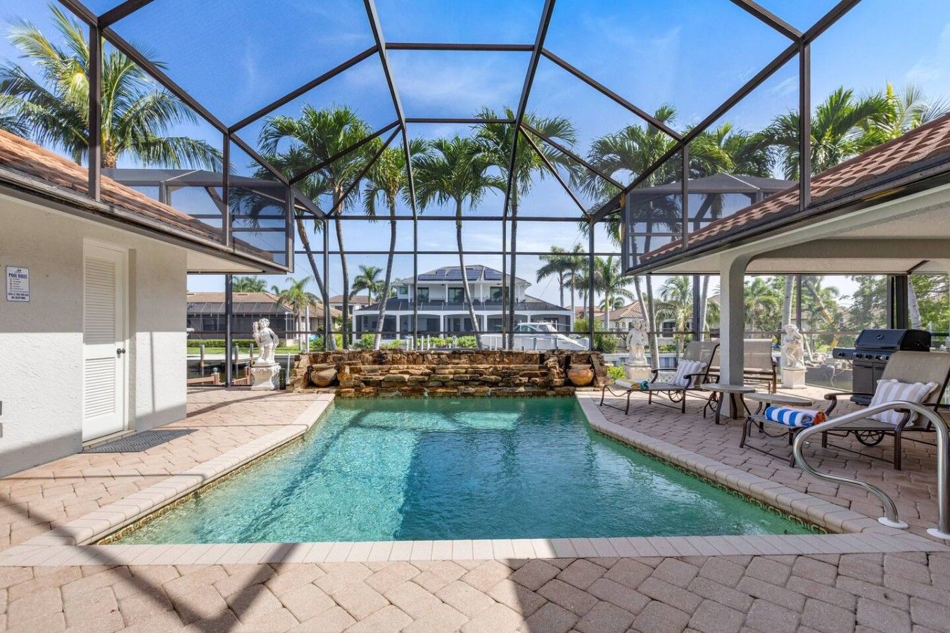 An indoor swimming pool with a glass ceiling, surrounded by lounge chairs and a stone waterfall feature.