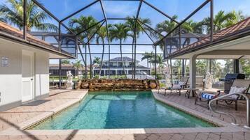 An indoor swimming pool with a glass ceiling, surrounded by lounge chairs and a stone waterfall feature.
