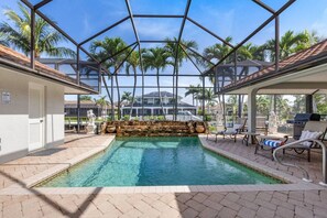 An indoor swimming pool with a glass ceiling, surrounded by lounge chairs and a stone waterfall feature. - Marco Island Antigua Villa • Dock • Walk to Beach (Marco Island)