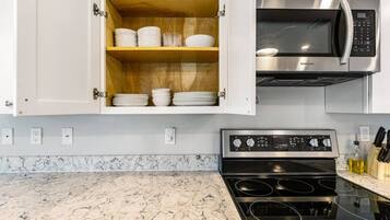 A kitchen with a built-in microwave, stove, and wooden storage cabinet with dishes.