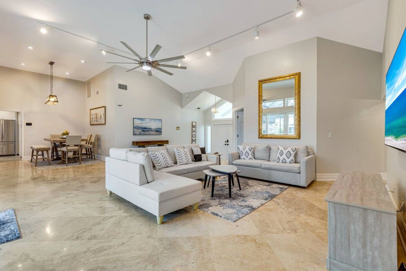 A spacious living area with a large L-shaped sofa, a dining table with chairs, and a ceiling fan.