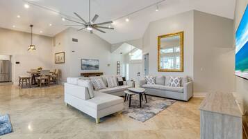 A spacious living area with a large L-shaped sofa, a dining table with chairs, and a ceiling fan.