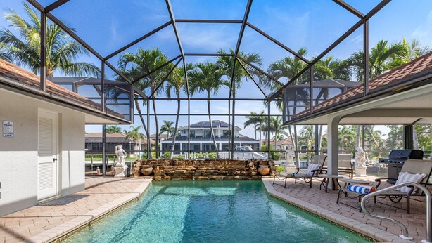 An indoor swimming pool with a glass ceiling, palm trees, and lounge chairs.