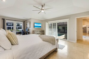 A bedroom with a large bed, a ceiling fan, a desk with a computer, and a view of a pool through a sliding door. - Marco Island Antigua Villa • Dock • Walk to Beach (Marco Island)