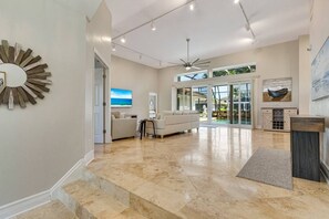 A spacious living area with a high ceiling, a ceiling fan, and a view of the outdoors through large glass doors.