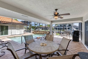 An outdoor patio with a round table, chairs, a ceiling fan, and a view of a swimming pool and boats. - Marco Island Antigua Villa • Dock • Walk to Beach (Marco Island)