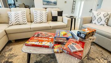 A living room with a sofa, a coffee table with board games, and a wall with a 'HOME' sign.