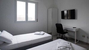 A hotel room with two beds, a desk, a chair, a wardrobe, and a TV.