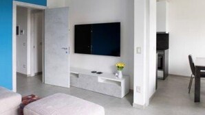 A modern living room with a flat-screen TV mounted on the wall, a white console table with a vase of flowers, and a dining area with a table and chairs.