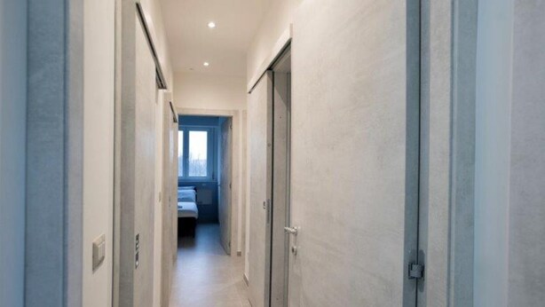 A narrow hallway with doors on both sides leading to a bedroom with a bed and a window.