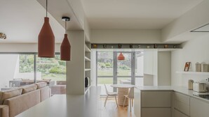 A modern kitchen with a large island, pendant lights, and a view of the garden.