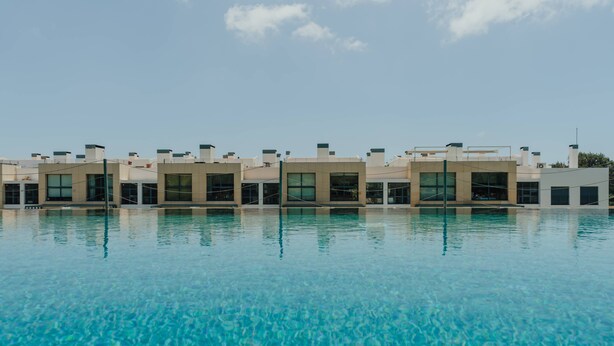 A swimming pool with clear blue water, surrounded by modern buildings with large windows and flat roofs.
