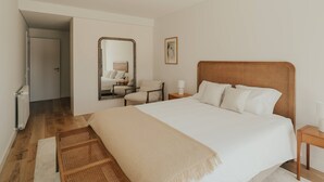 A bedroom with a large bed, a wooden headboard, a bedside table with a lamp, a mirror, and a chair.