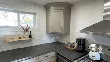 Una cocina moderna con armarios grises, una estufa de acero inoxidable y una ventana con vista a árboles.