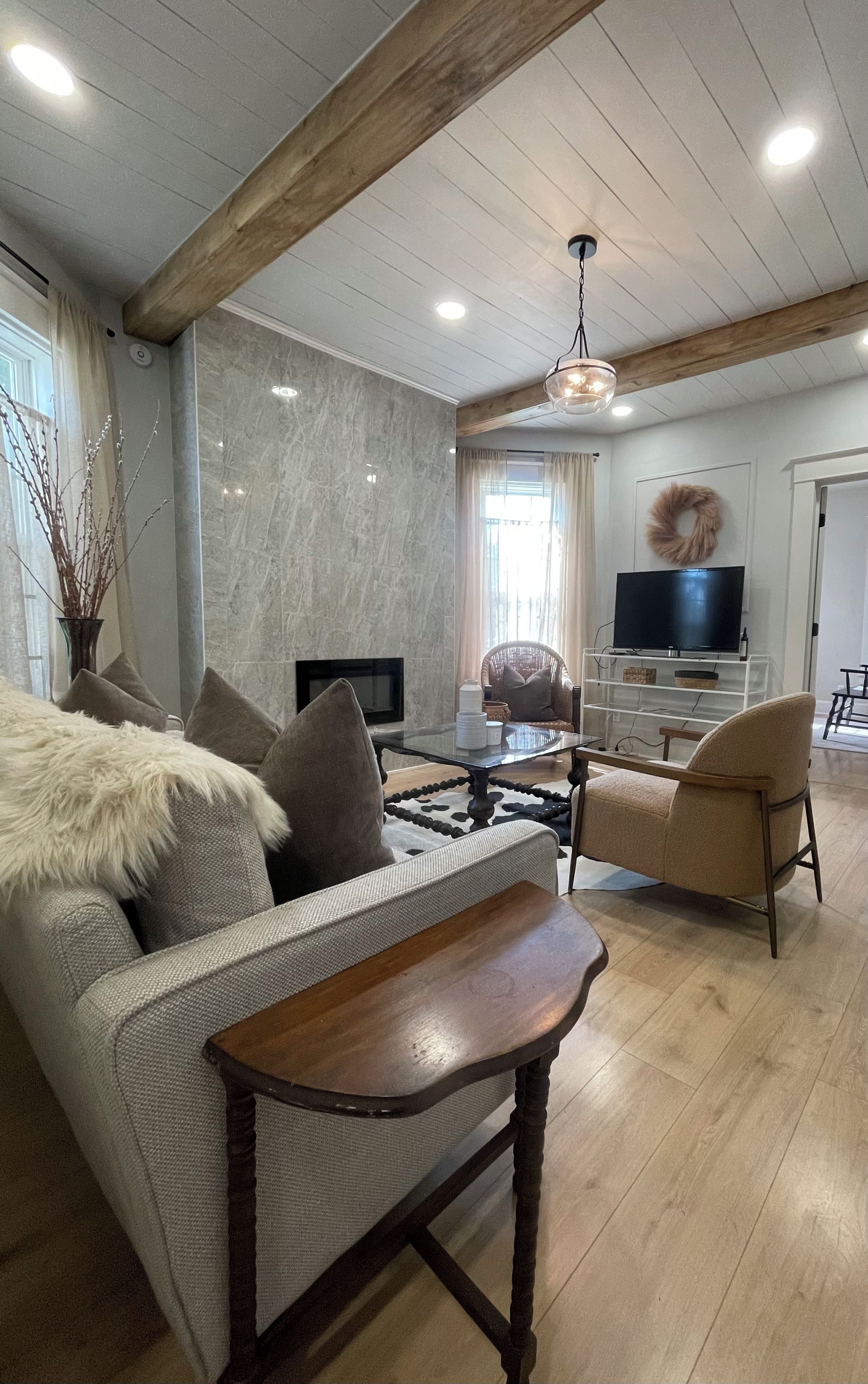 A modern living room with a sofa, armchair, wooden coffee table, and a television.