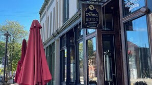 Un edificio con un letrero que indica Alma Brewing Co. y mesas al aire libre con sombrillas rojas.