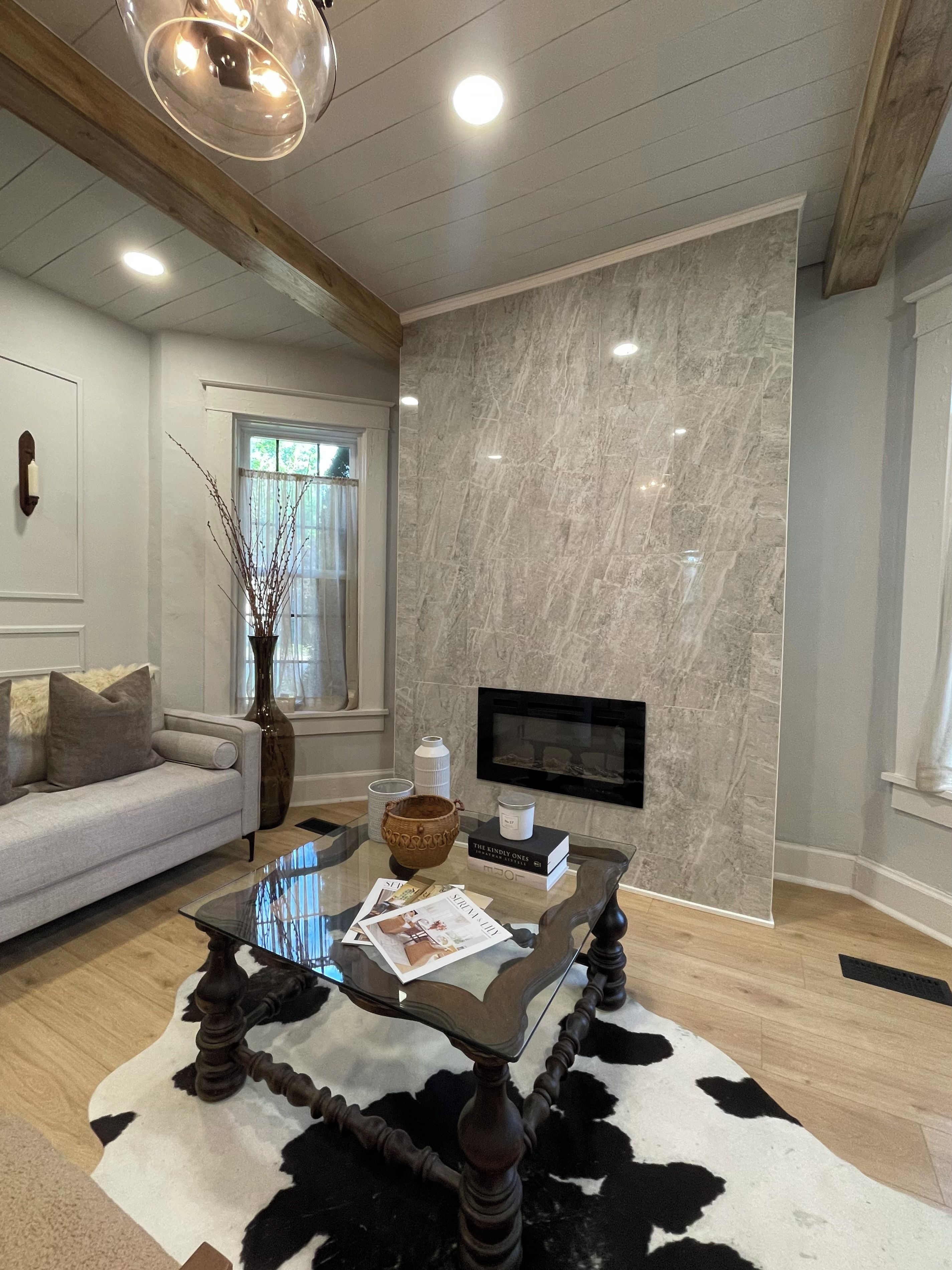 A modern living room with a marble wall, a fireplace, a glass coffee table, and a cowhide rug.