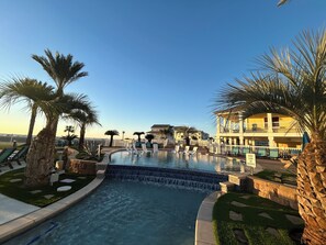 Una piscina con cascada, rodeada de palmeras y sillones de descanso.