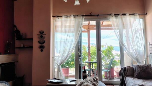 A room with a large window, a table with a bottle of wine, and a sofa. -     Καλώς ήρθατε στη βάση των διακοπών σας. (Κόρινθος)