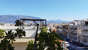 A rooftop terrace with a pergola, surrounded by buildings and mountains in the background. -     Καλώς ήρθατε στη βάση των διακοπών σας. (Κόρινθος)