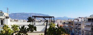 A rooftop terrace with a pergola, surrounded by buildings and mountains in the background.