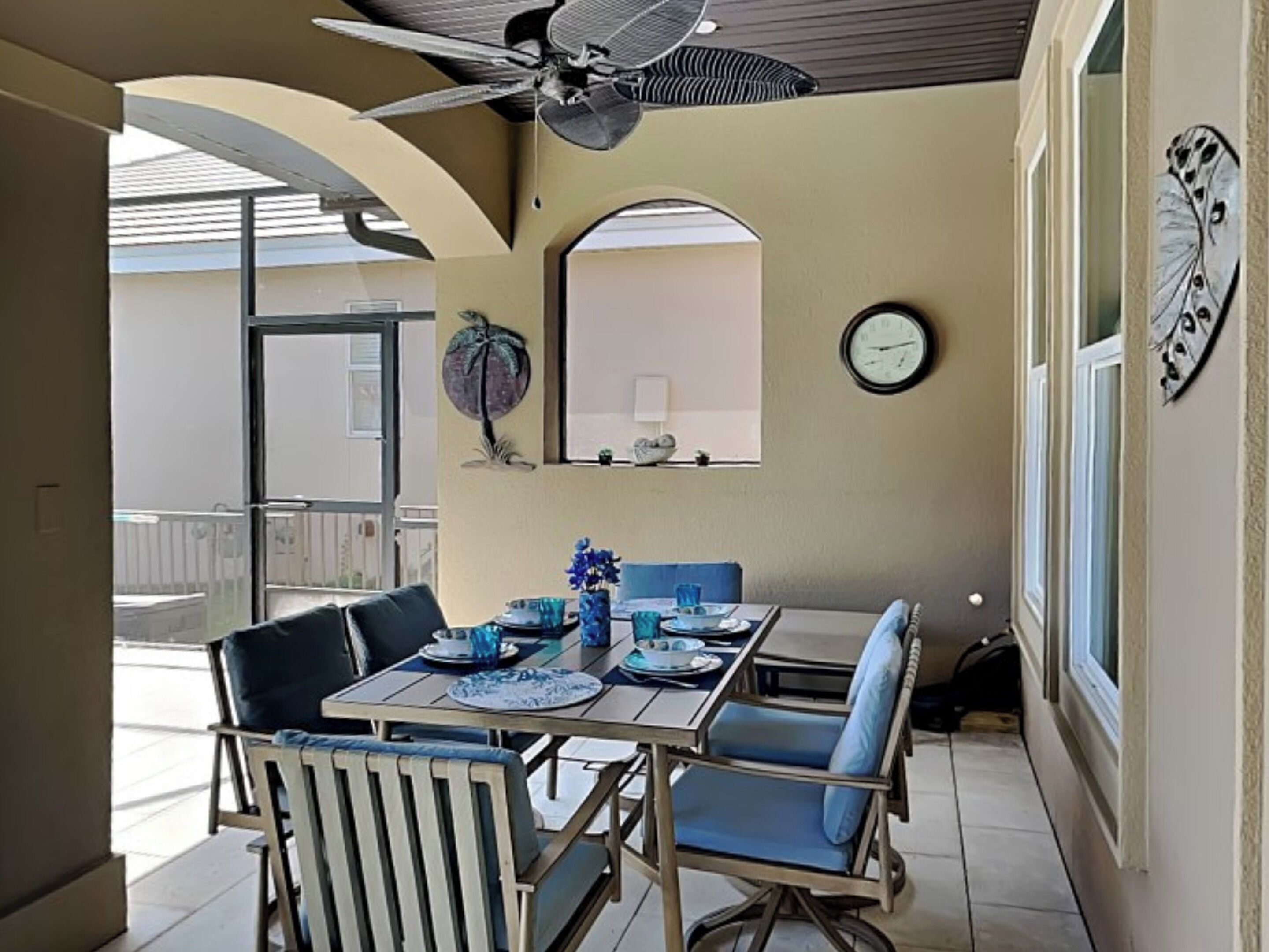 Un comedor con una mesa dispuesta para cuatro, ventilador de techo, un reloj y un adorno en la pared.