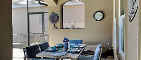 Un comedor con una mesa dispuesta para cuatro, ventilador de techo, un reloj y un adorno en la pared.