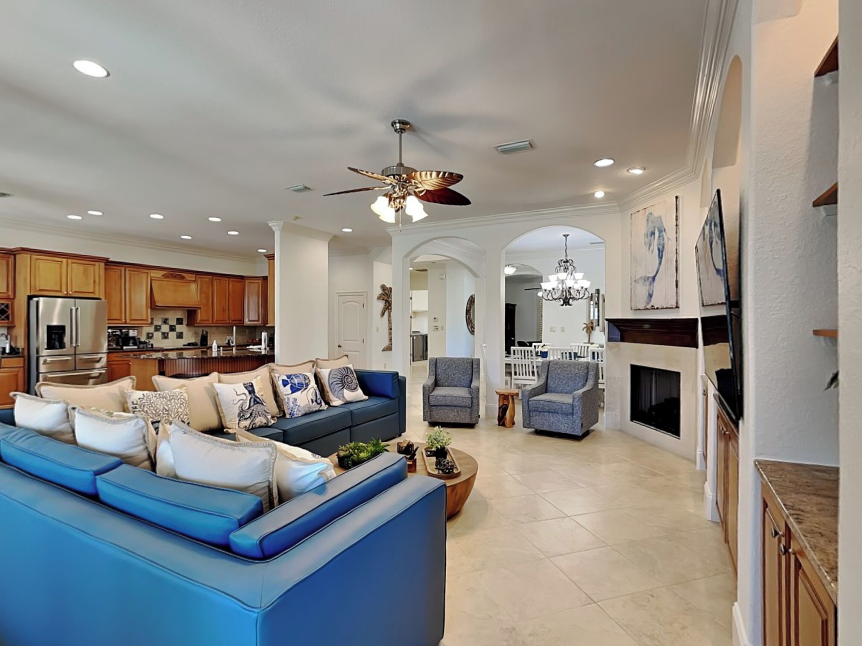 A spacious living room with a blue sectional sofa, a fireplace, and a kitchen in the background.